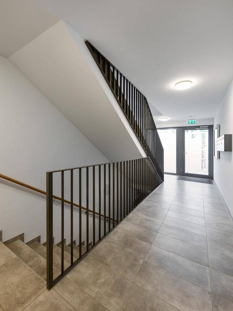 Moderner Flur mit Treppenhaus und Fliesenboden im Eingangsbereich des Gebäudes.