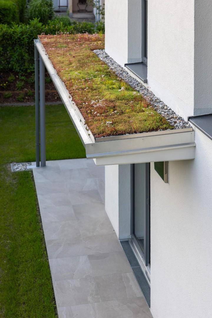 Detailansicht der modernen Fassade mit begrüntem Dach und gepflastertem Gehweg.