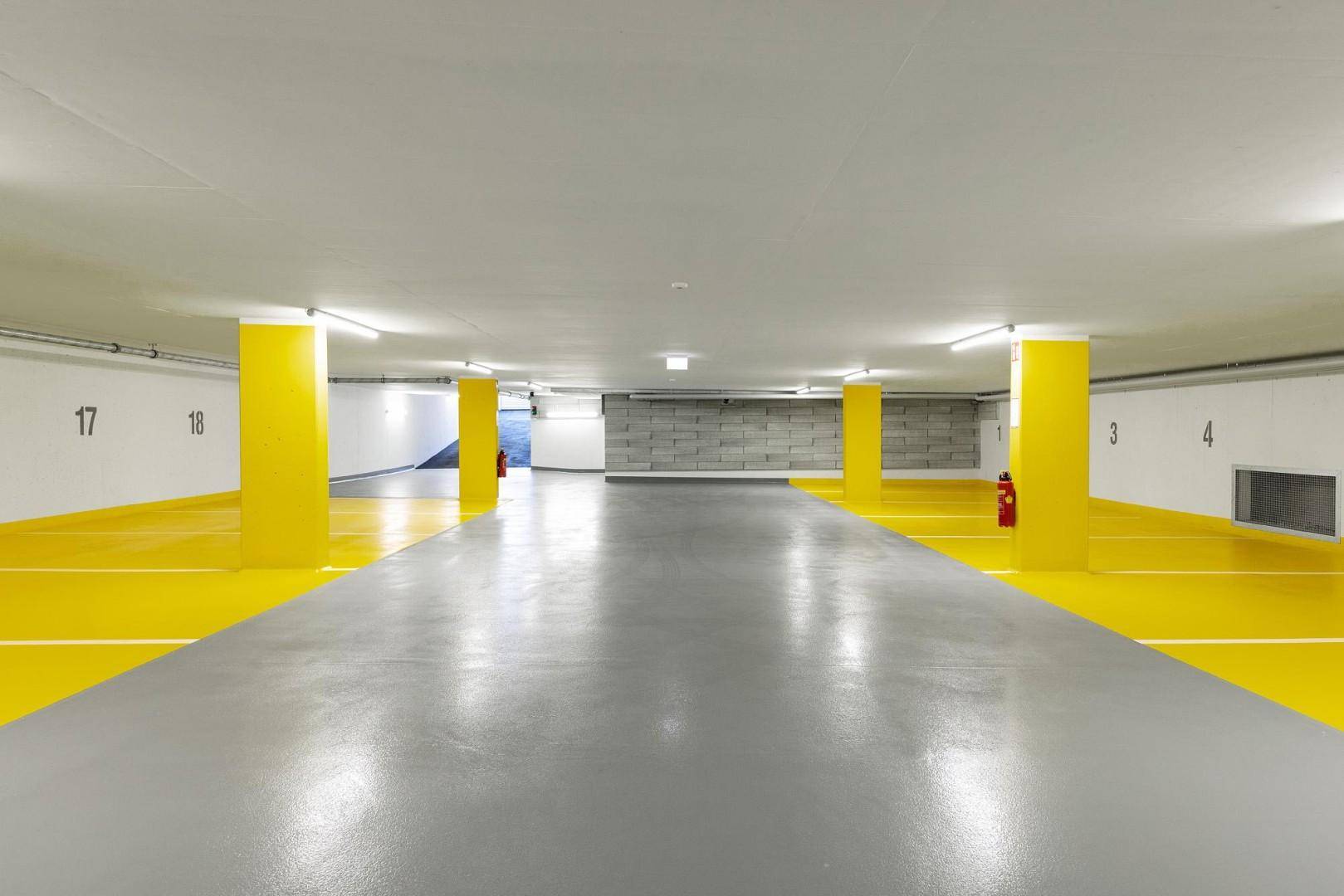 Geräumige Tiefgarage mit markierten Stellplätzen und leuchtend gelben Säulen.