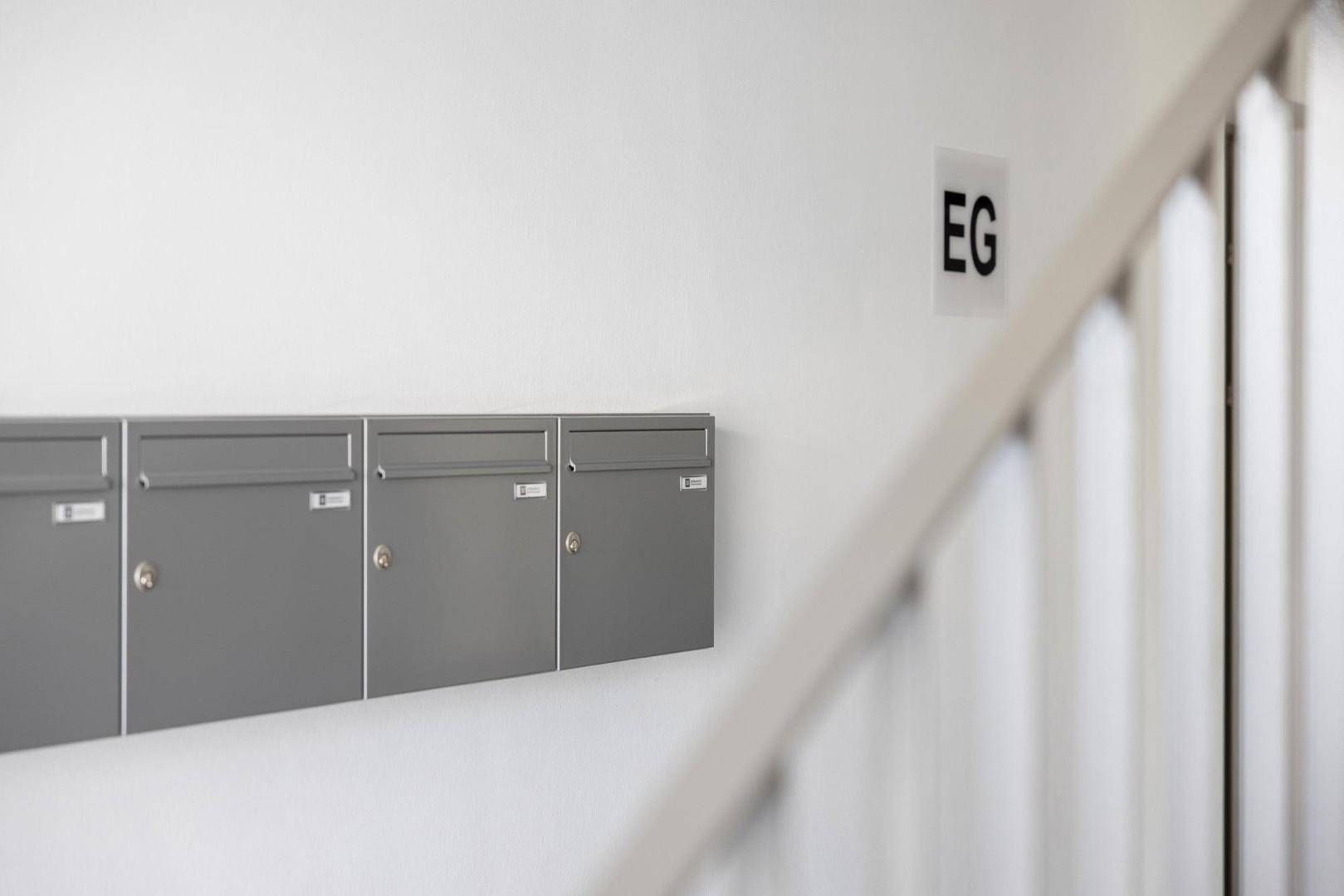 Reihe von modernen Briefkästen an einer weißen Wand im Eingangsbereich eines Mehrfamilienhauses.