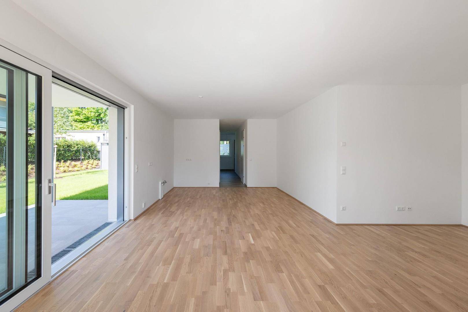 Heller, leerer Raum mit Holzboden und großen Schiebetüren zum Garten.