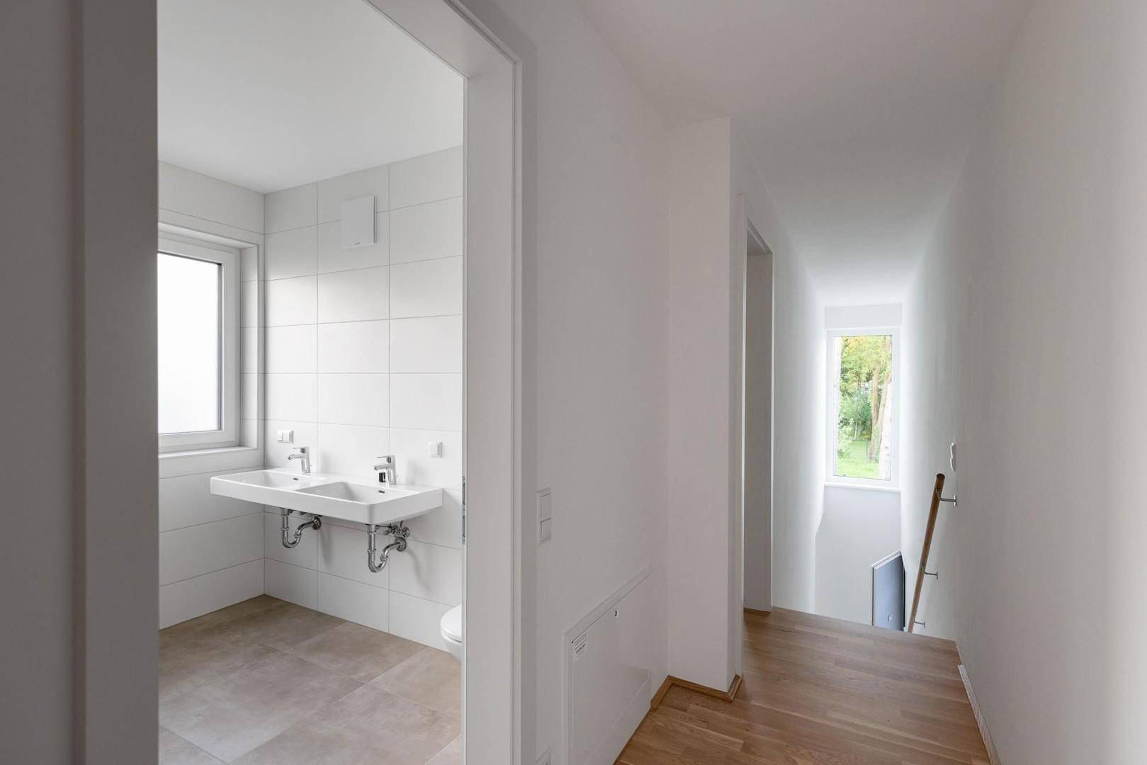 Heller Flur mit Holzfußboden, der zu einem modernen Badezimmer mit Doppelwaschbecken führt.