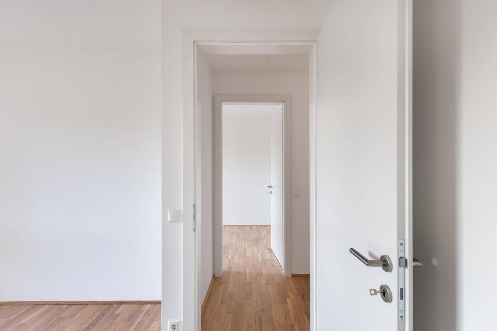 Leerer Flur mit hellem Holzfußboden und offenen Türen, die den Blick in weitere Räume freigeben.
