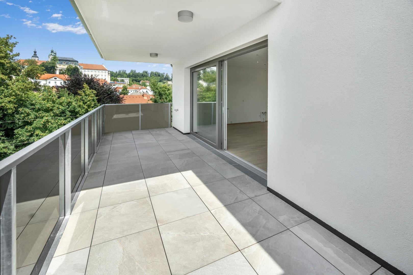 Geräumiger Balkon mit Fliesenboden und Glasgeländer, bietet einen weiten Blick über die Stadt.