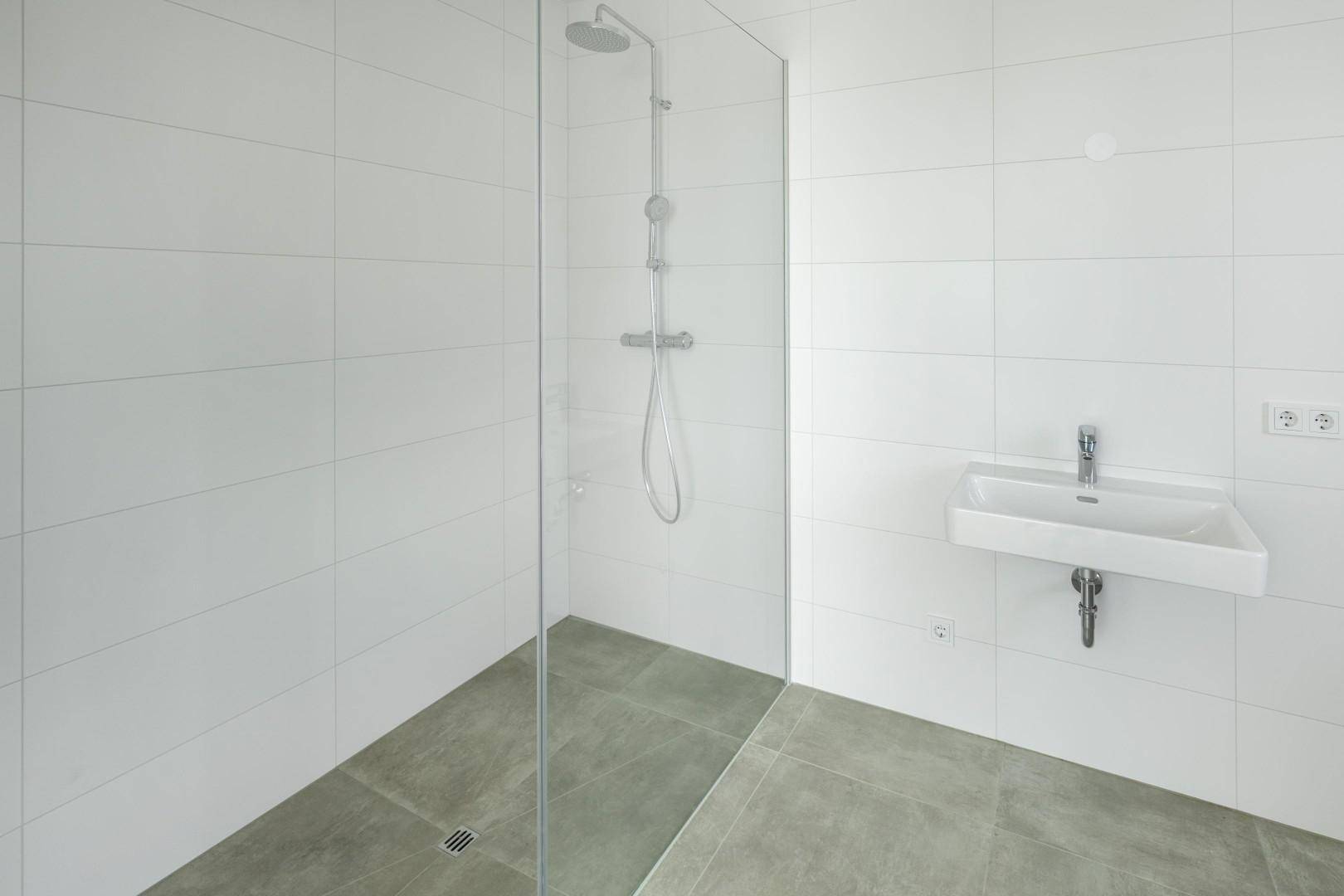Modernes Badezimmer mit weiß gefliesten Wänden, ebenerdiger Dusche und Einzelwaschbecken.