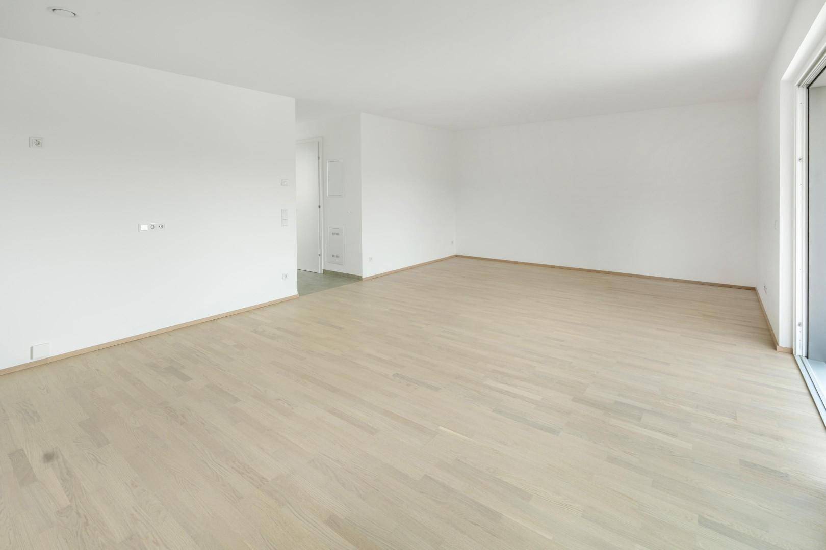 Geräumiges Wohnzimmer mit hellem Holzparkett und weiß gestrichenen Wänden, bereit zur Einrichtung.