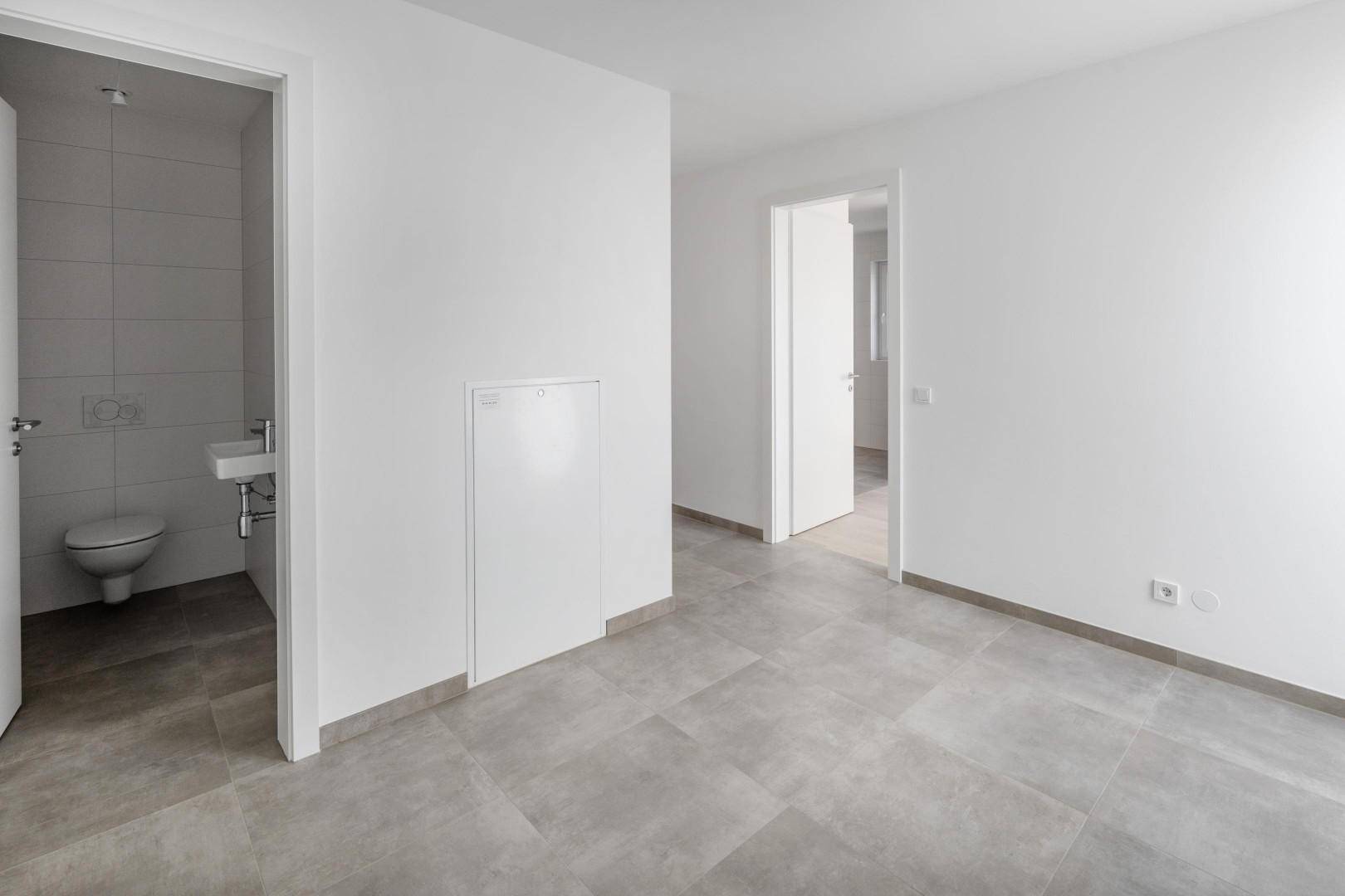 Heller Flur mit grauen Fliesen und Zugang zu einem separaten Gäste-WC.