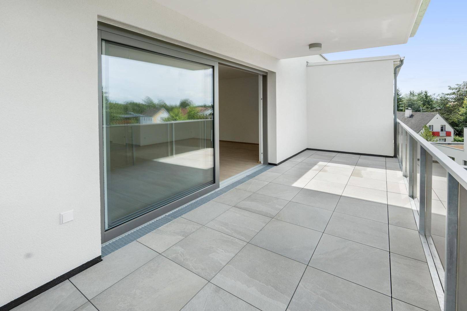 Heller Balkon mit modernen Fliesen und Schiebetüren, die Zugang zum Innenbereich bieten.