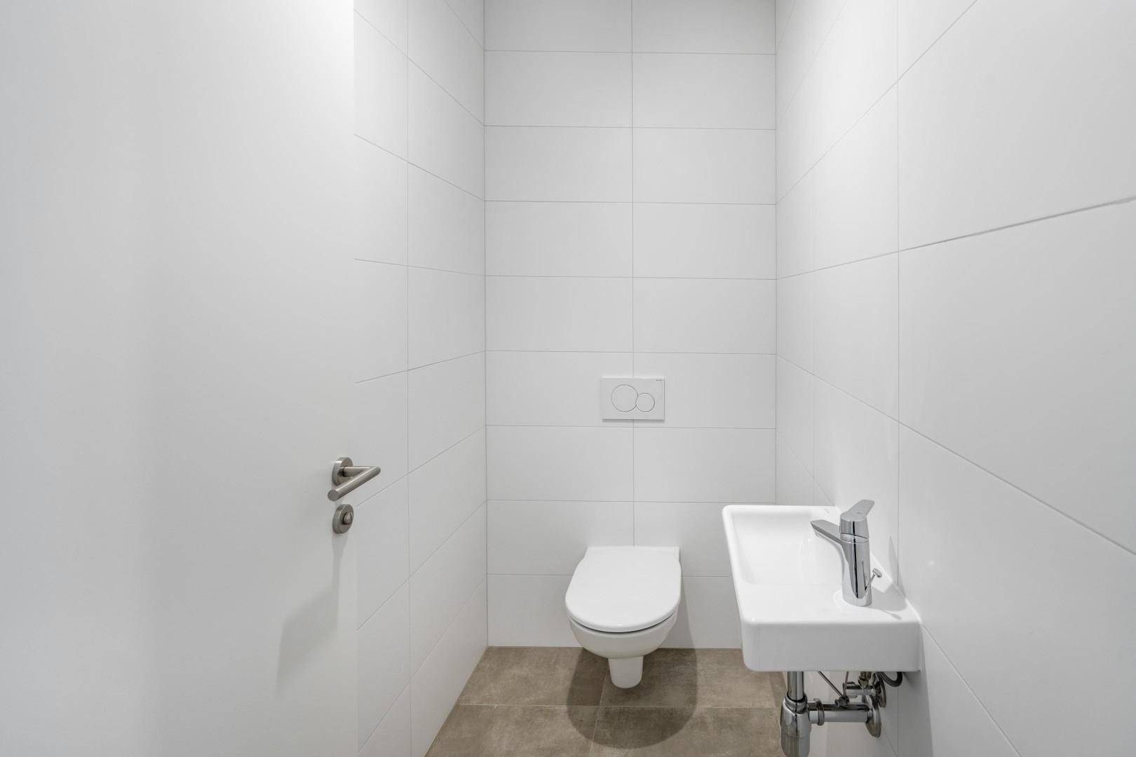 Modernes Gäste-WC mit weißen Fliesen, wandhängendem WC und kleinem Waschbecken.
