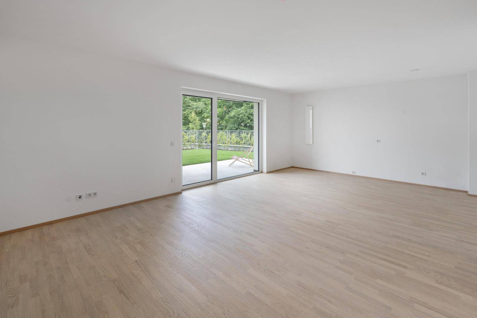 Geräumiges Wohnzimmer mit hellem Holzfußboden und großer Schiebetür zum Gartenbereich.