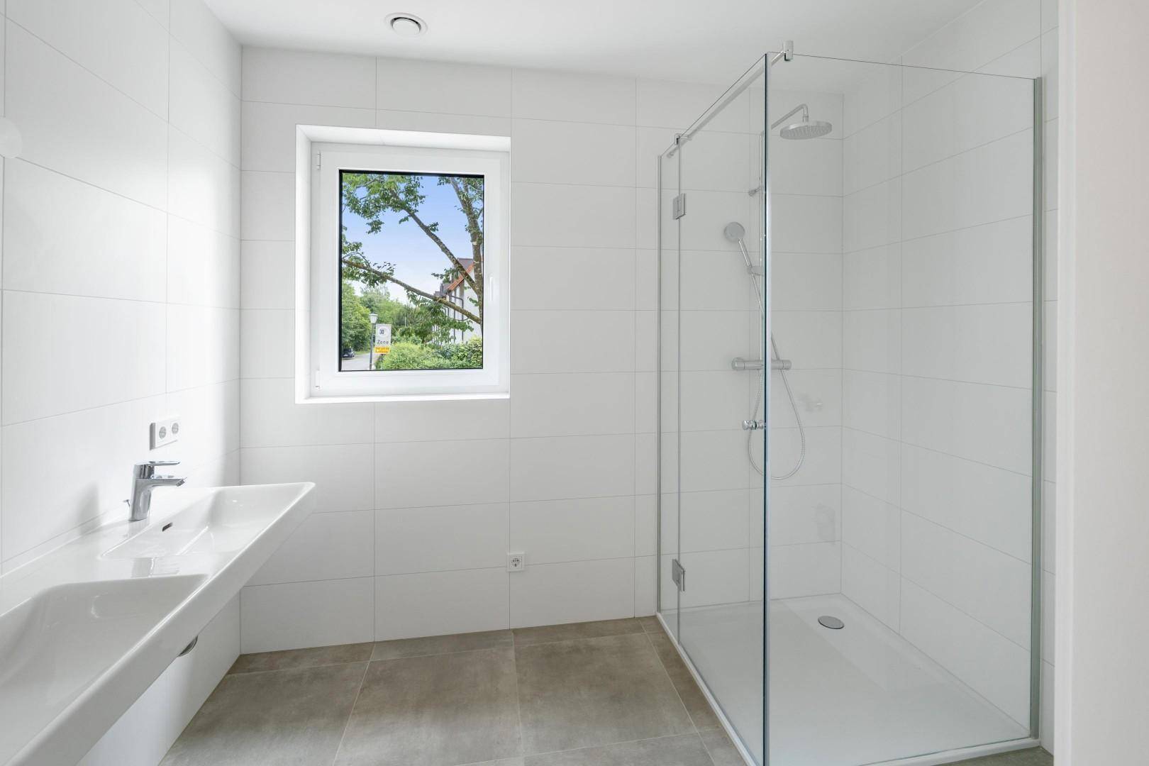 Modernes Badezimmer mit weißen Fliesen, ebenerdiger Dusche und Fenster für Tageslicht.