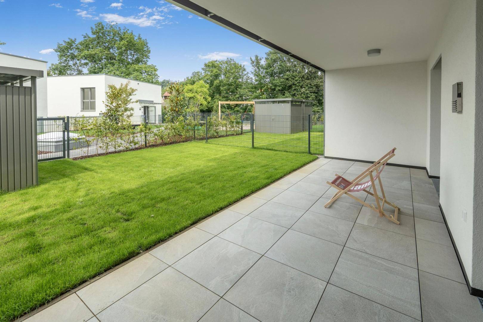 Geräumige Terrasse mit Fliesenboden und angrenzendem Rasenbereich, ideal für Entspannung im Freien.