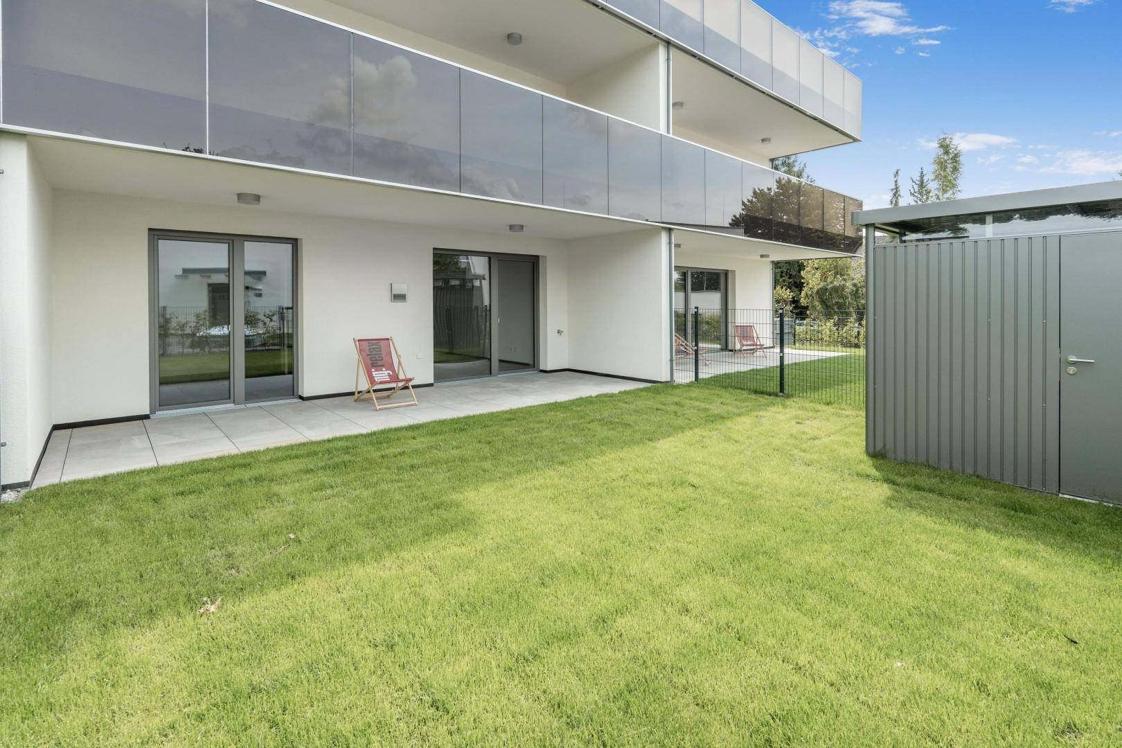 Erdgeschoss-Terrasse mit Rasenfläche und Zugang zu den Wohnräumen eines modernen Gebäudes.