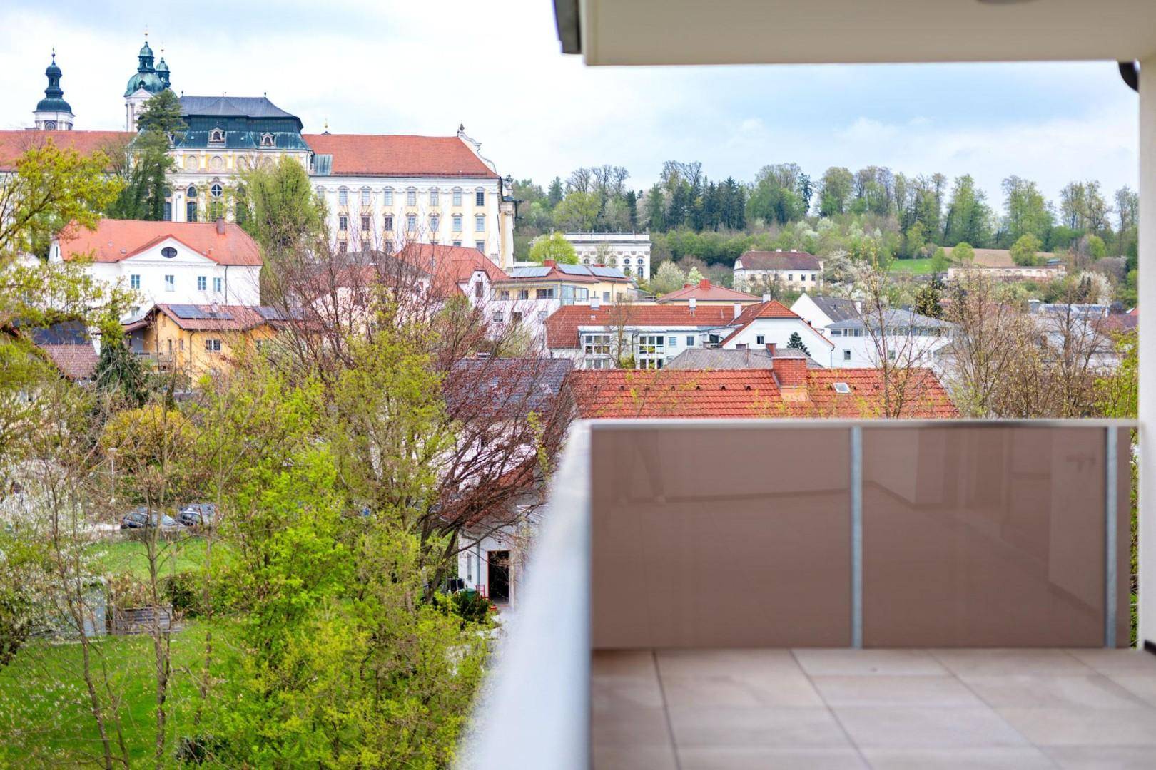 Panoramablick vom Balkon über eine historische Stadt mit beeindruckendem Klostergebäude und viel Grün.