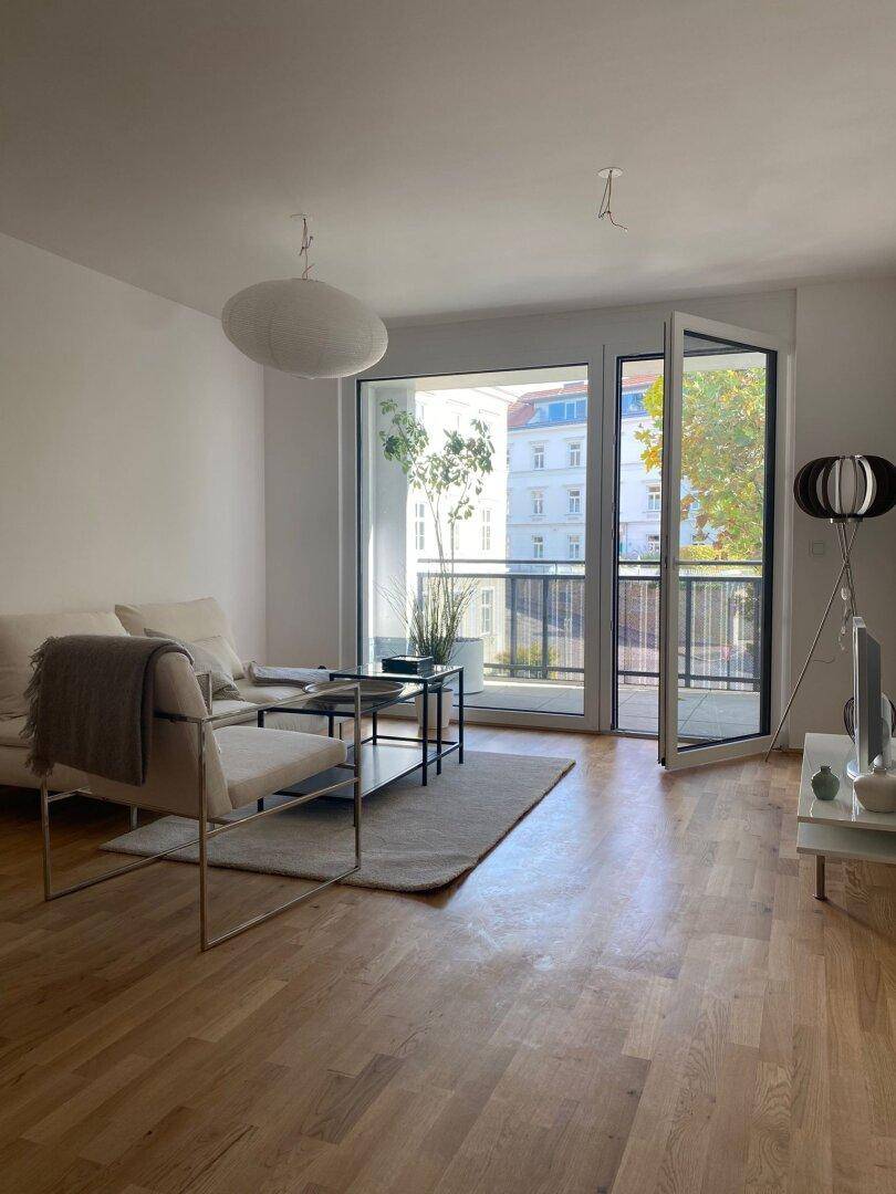 Helles Wohnzimmer mit Holzboden, modernen Möbeln und Zugang zu einem Balkon.