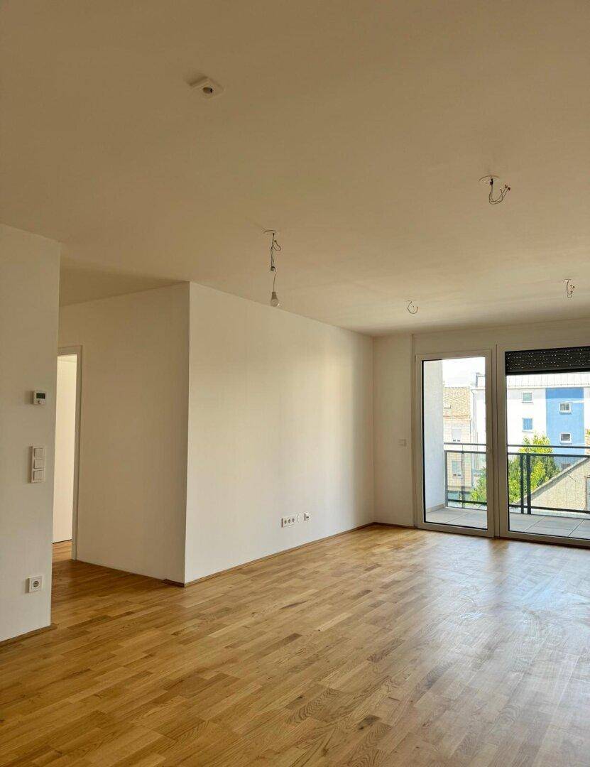 Geräumiger, unmöblierter Wohnbereich mit Parkettboden und Zugang zu einem Außenbereich.