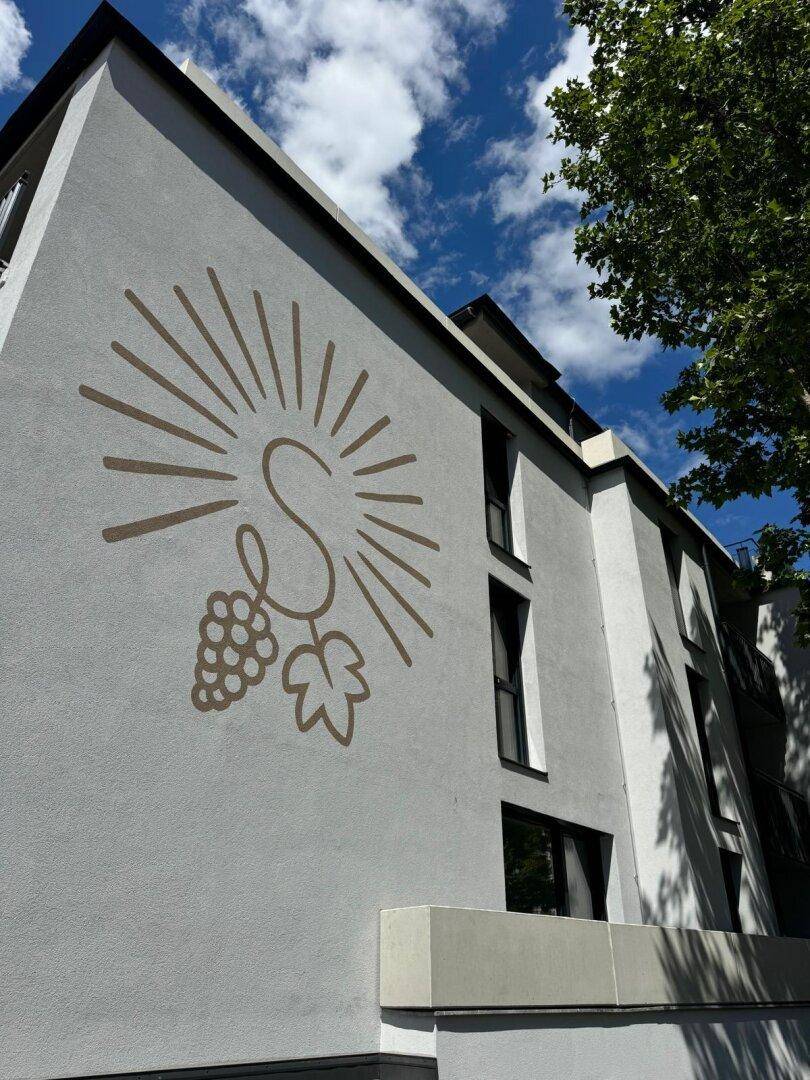 Moderne Gebäudefassade mit einem dekorativen Logo und klaren architektonischen Linien unter blauem Himmel.