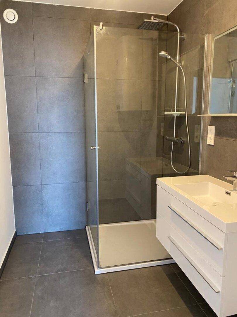 Modernes Badezimmer mit großformatigen grauen Fliesen, einer begehbaren Dusche und einem Einzelwaschbecken.