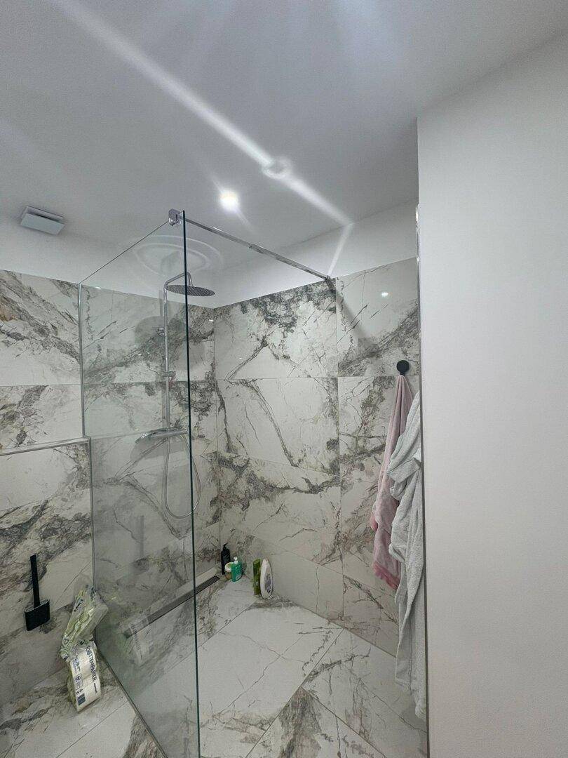 Moderne Dusche mit großformatigen Marmor-Optik-Fliesen und Glasabtrennung.