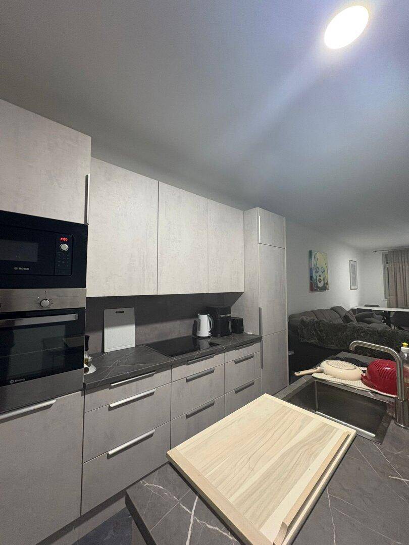 Moderne Einbauküche mit grauen Schränken, integrierten Geräten und dunkler Arbeitsplatte.