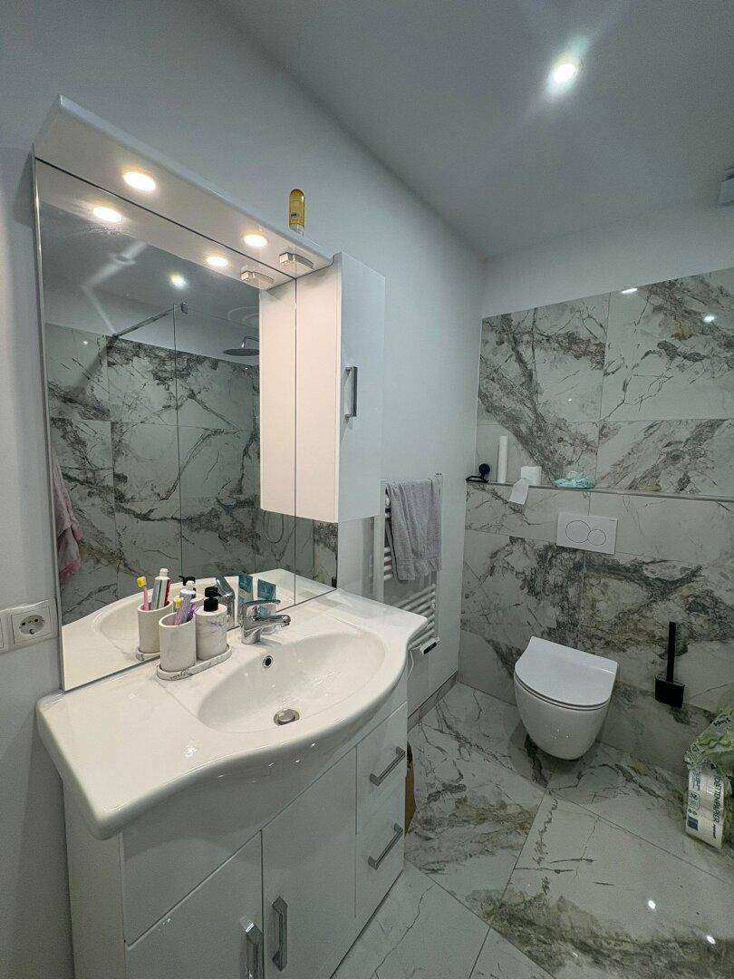 Helles Badezimmer mit modernem Waschtisch, Spiegelschrank, wandhängendem WC und Marmor-Optik-Fliesen.