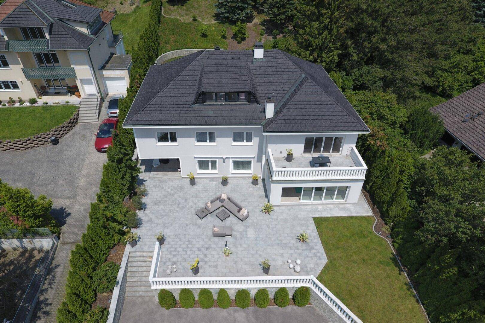 Luftaufnahme des Hauses mit großer gepflasterter Terrasse, Sitzgelegenheiten und weitläufigem Gartenbereich.