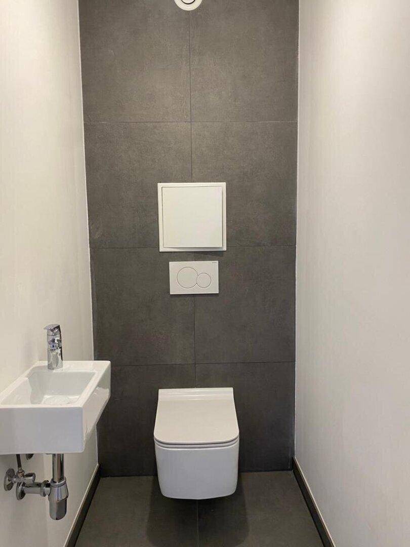 Modernes Gäste-WC mit dunklen Fliesen, wandhängendem WC und kleinem Waschbecken.
