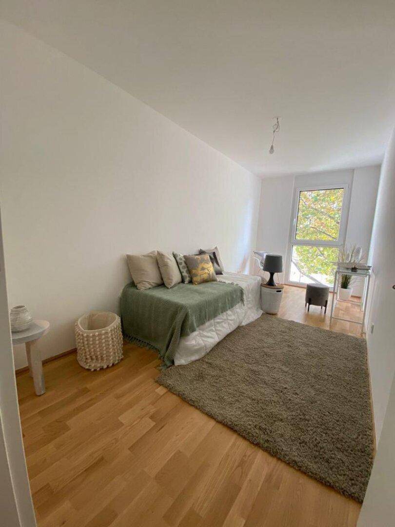 Gemütliches Schlafzimmer mit Holzboden, Teppich und viel Tageslicht durch das große Fenster.