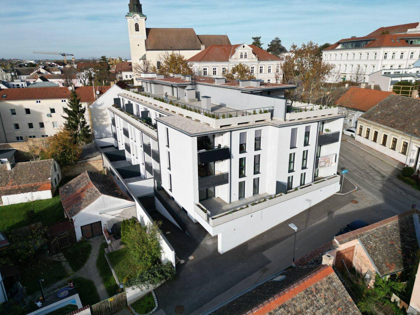 Moderne Wohnanlage mit weißer Fassade und Flachdach in städtischer Umgebung, mit Blick auf eine Kirche.