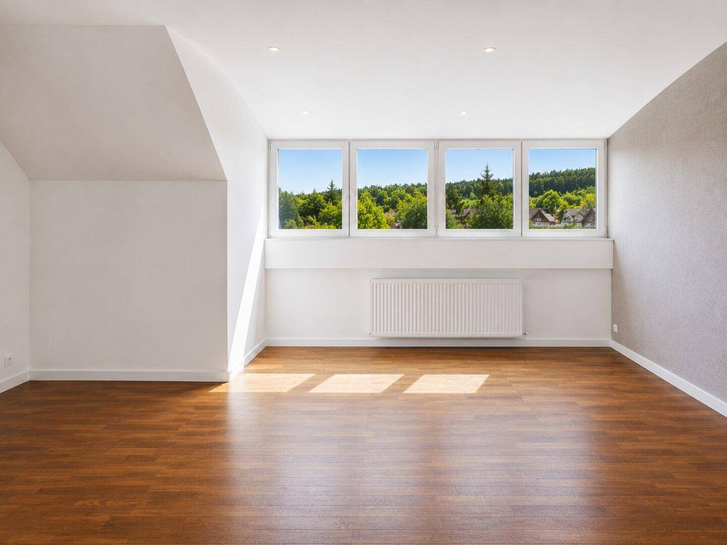 Heller Dachgeschossraum mit Holzfußboden und mehreren Fenstern, die einen weiten Blick ins Grüne bieten.