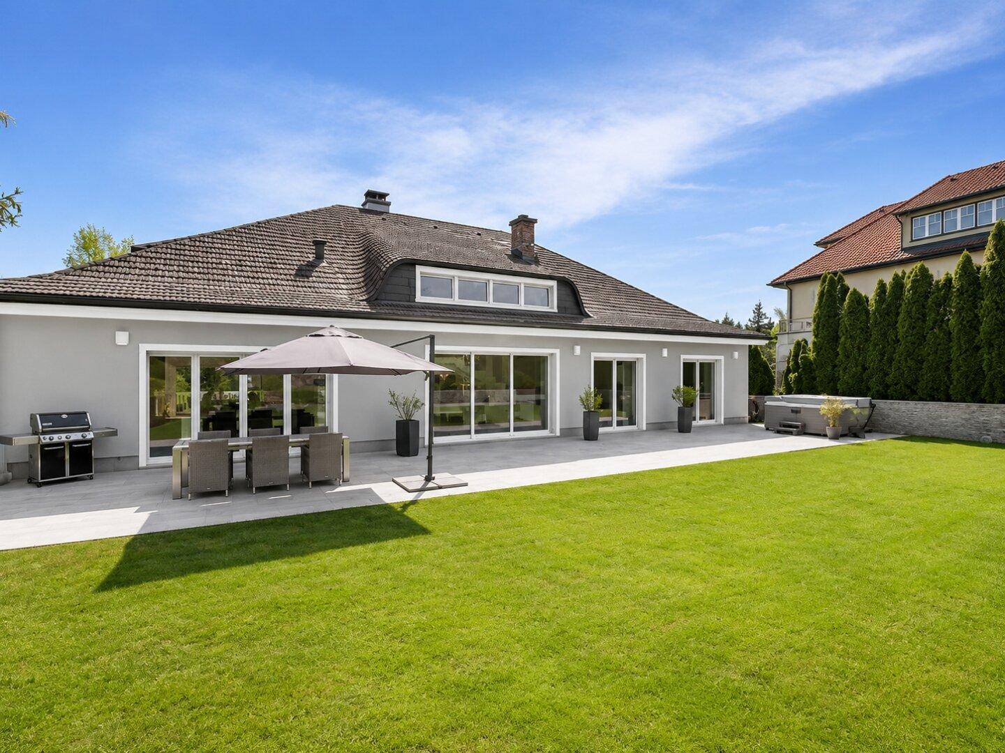 Hinteransicht des Hauses mit weitläufigem Rasen, großer Terrasse, Grillbereich und Whirlpool im Freien.