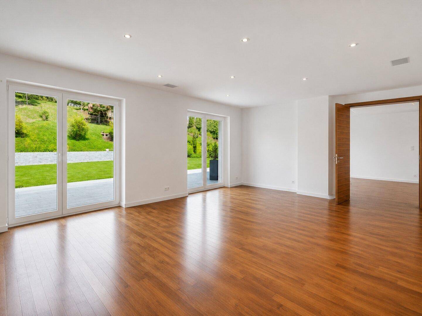 Geräumiges Wohnzimmer mit Holzboden, Einbaustrahlern und großen Glastüren zum Garten.