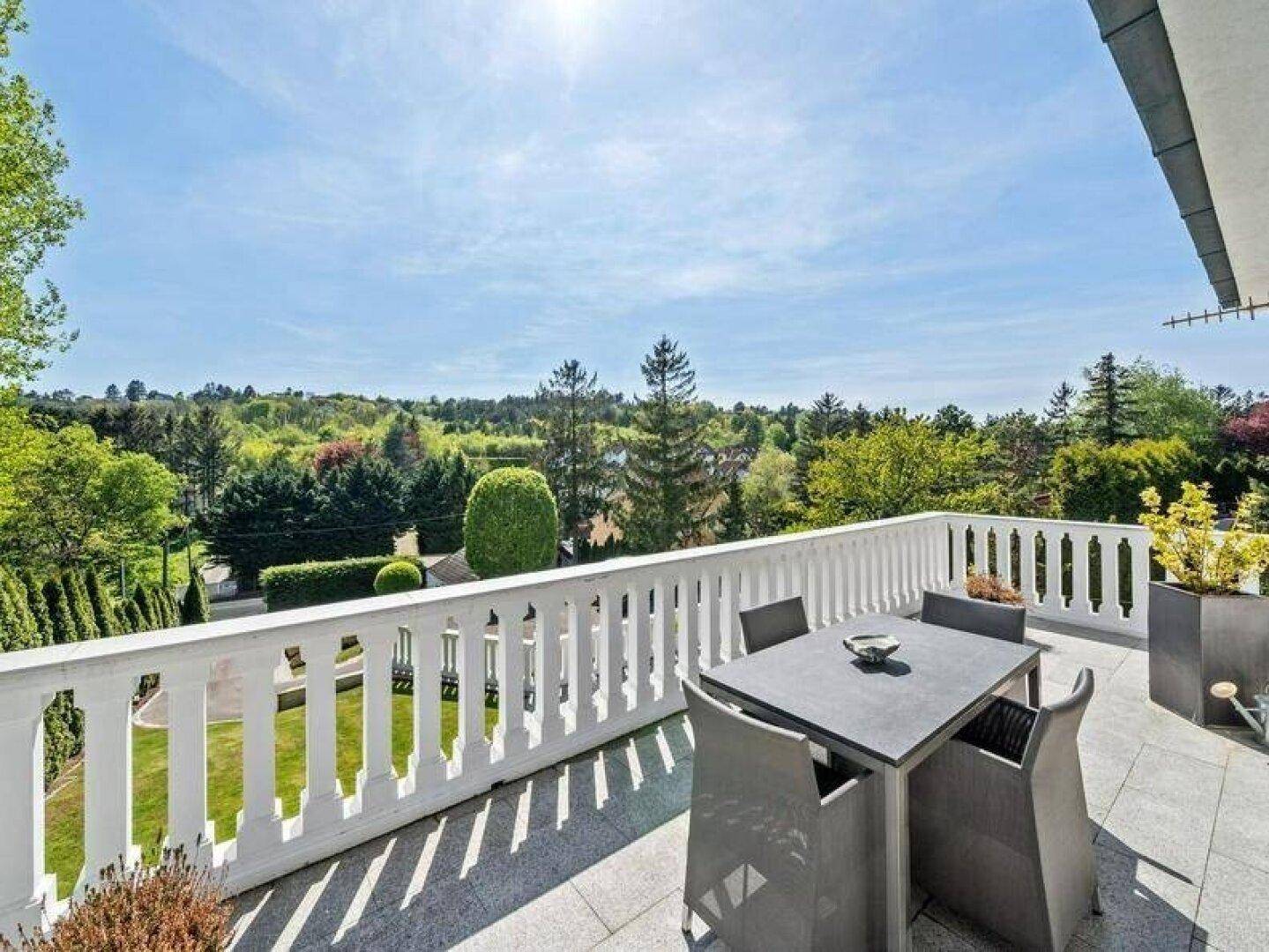 Großer Balkon mit Sitzgelegenheiten und weitem Blick über grüne Hügel und Baumlandschaften.