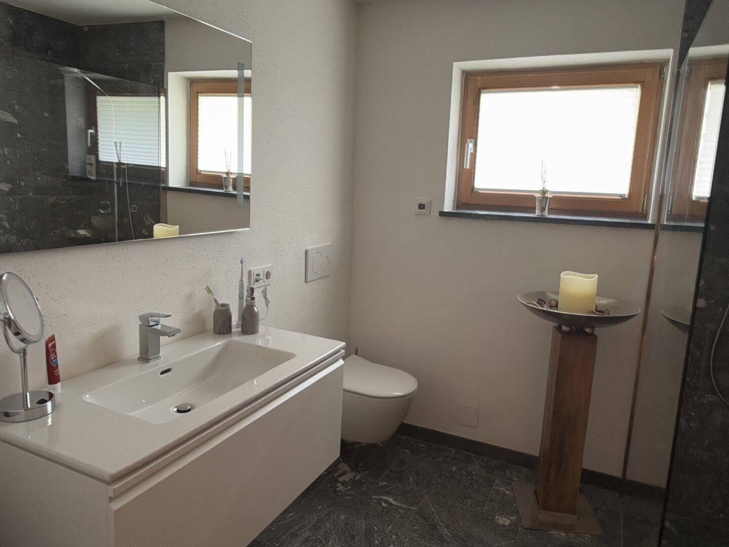 Helles Badezimmer mit modernem Waschtisch, Dusche und Fenster für Tageslicht.