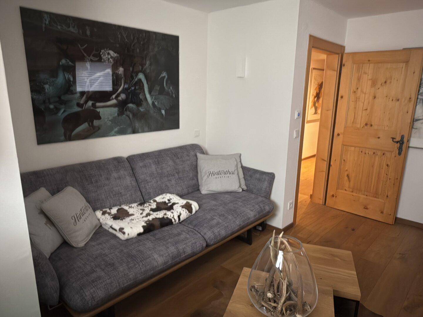 Gemütlicher Wohnbereich mit Sofa, Holzboden und großem Kunstwerk an der Wand.
