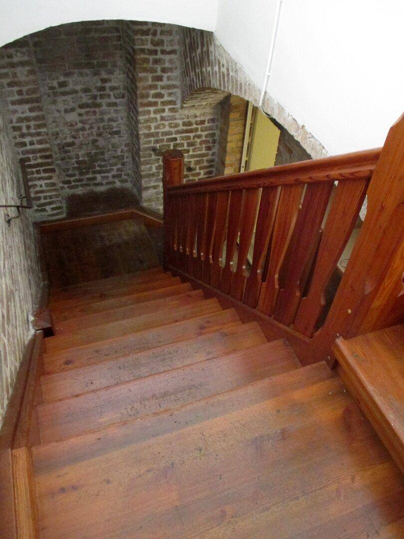 Rustikale Holztreppe mit passendem Geländer führt hinunter in einen Bereich mit Ziegelwänden, verbindet die Ebenen.