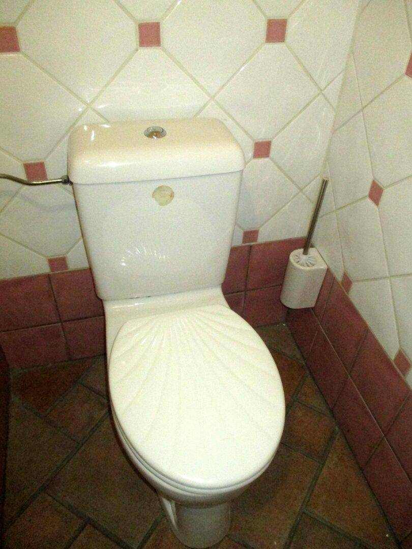 Toilettenbereich mit weißer Keramik und auffälligen weiß-rosa Fliesen an den Wänden, dazu Terrakotta-Bodenfliesen.