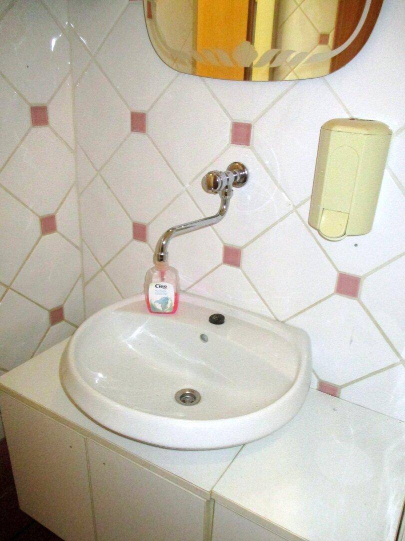 Waschbeckenbereich mit weißem Aufsatzwaschbecken auf einem Schrank, umgeben von weiß-rosa Wandfliesen und einem Spiegel.