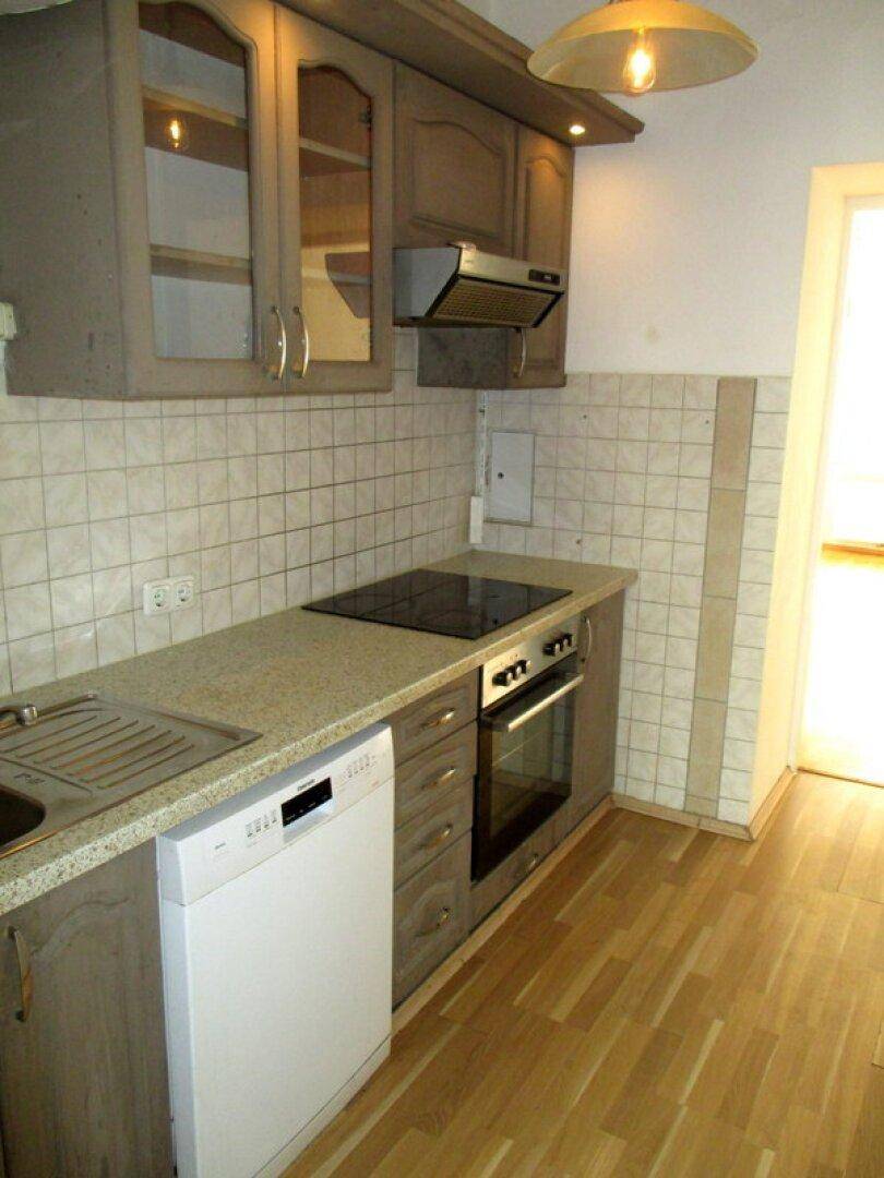 Funktionale Küche mit hellbraunen Schränken, Fliesenrückwand, Einbaugeräten und Laminatboden.
