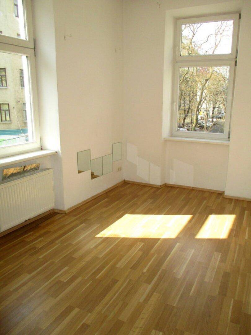 Helles Zimmer mit Laminatboden, weißen Wänden und dekorativen Spiegeln, die das Tageslicht reflektieren.