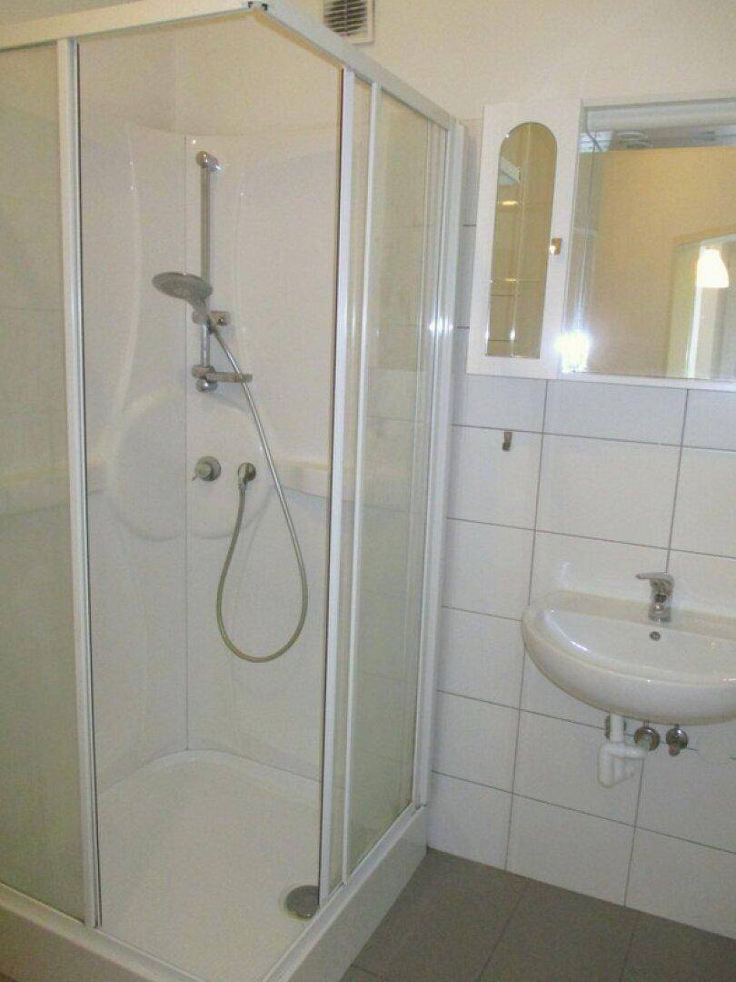 Badezimmer mit Duschkabine, kleinem Waschbecken, Spiegelschrank und hellen Fliesen an den Wänden.