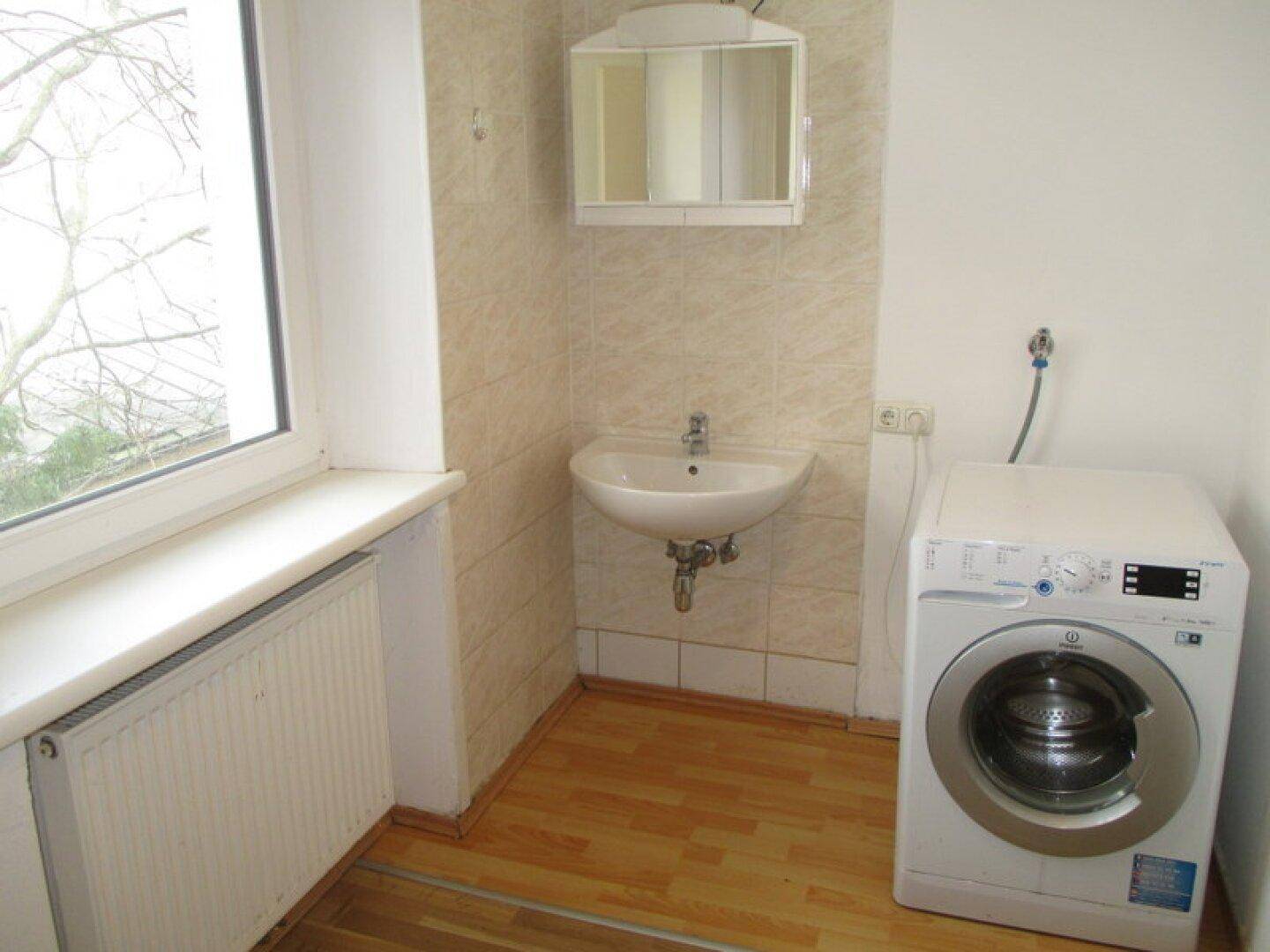 Praktischer Hauswirtschaftsraum mit Waschmaschine, kleinem Waschbecken, Spiegelschrank und Fenster.