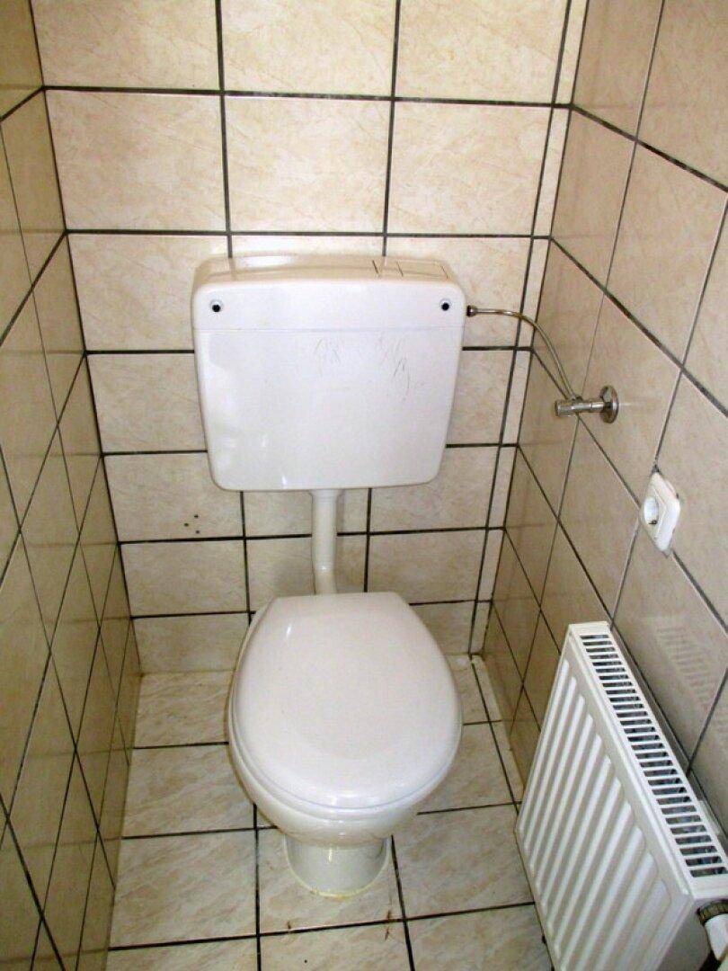 Kleines WC mit Toilette, Heizkörper und hellen Fliesen an Wänden und Boden.