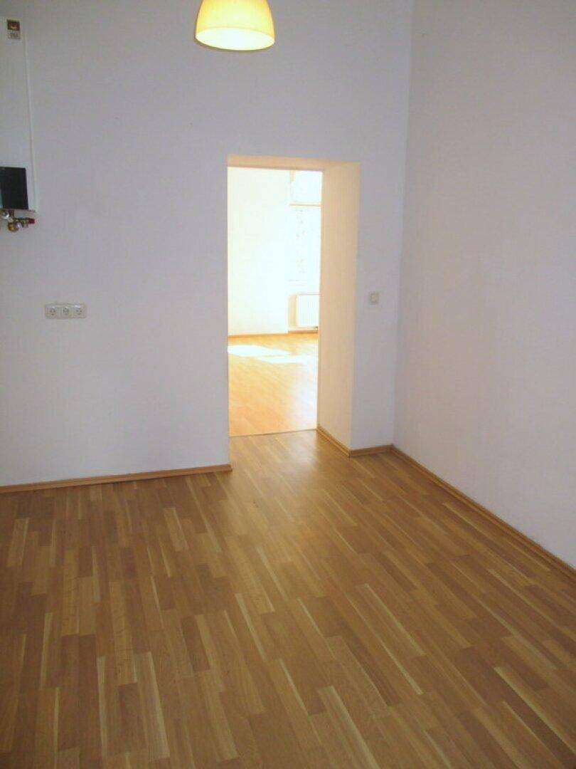 Heller Flur mit Laminatboden und weiß gestrichenen Wänden, der zu einem weiteren Zimmer führt.
