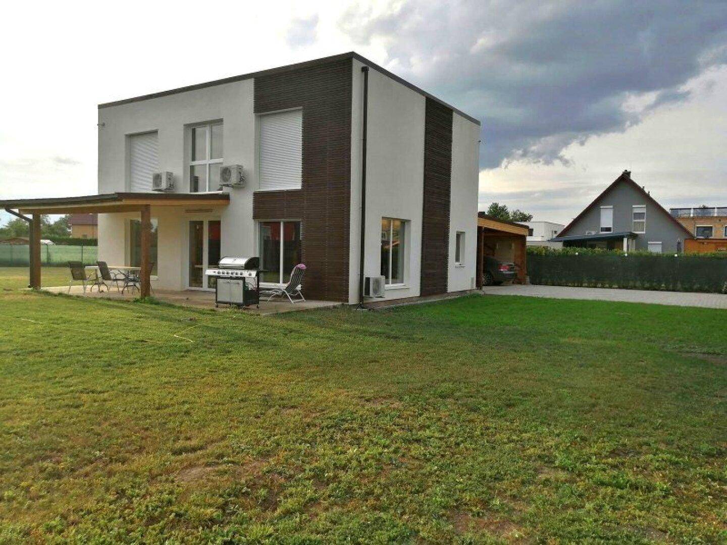 Modernes Haus mit weißer und brauner Fassade, großem Garten und überdachter Terrasse mit Grill.