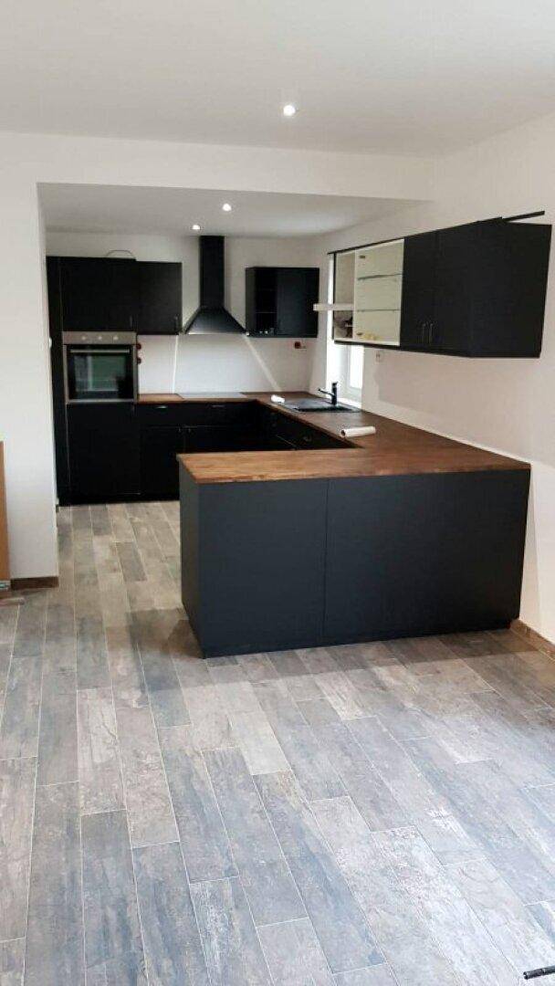 Moderne Küche mit schwarzen Schränken, Holz-Arbeitsplatten und integrierten Geräten.