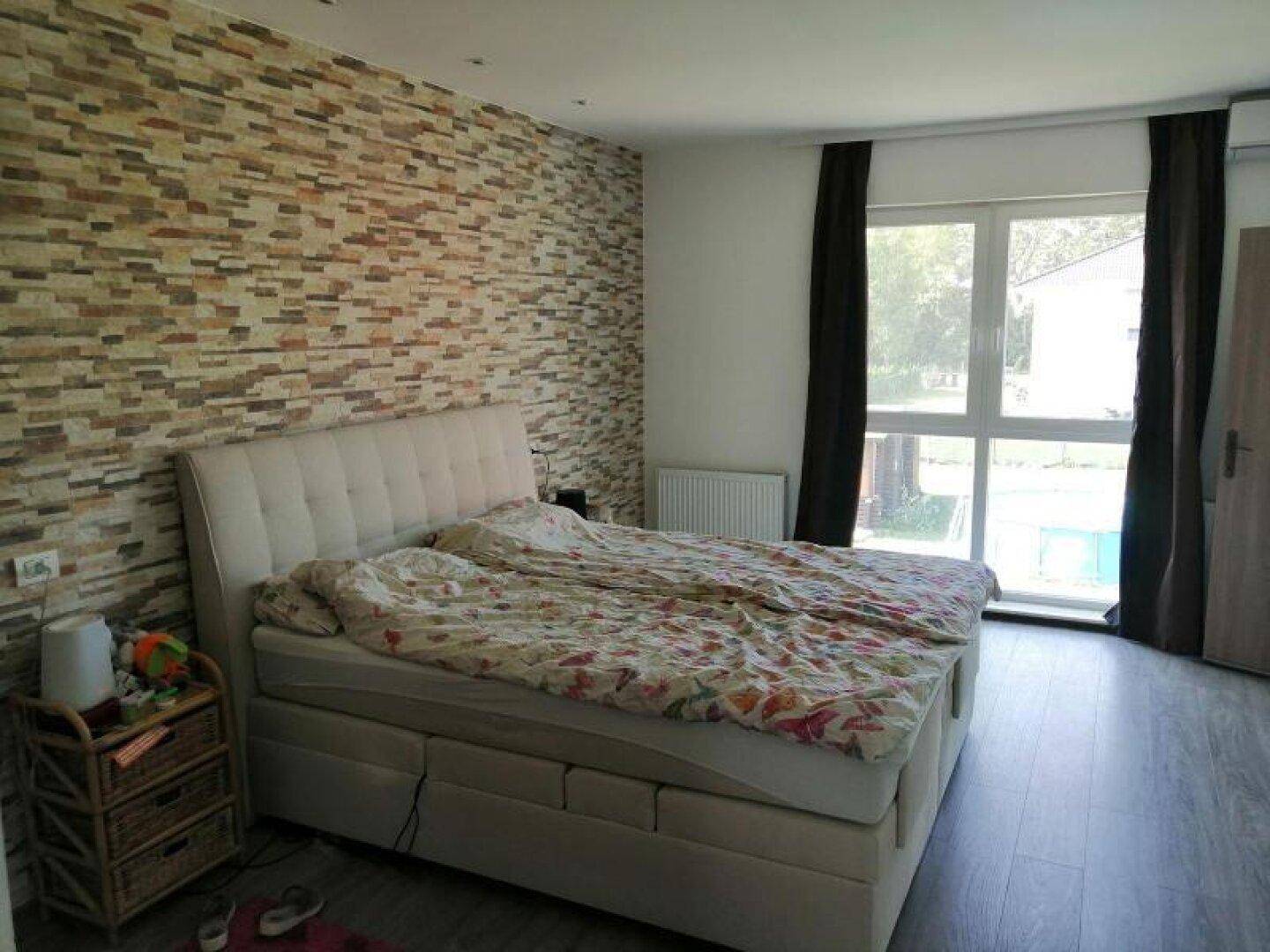Schlafzimmer mit großem Bett, Steinwand und Zugang zum Außenbereich mit Pool.