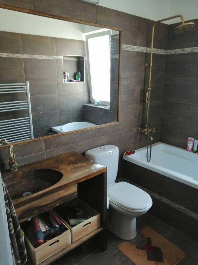 Badezimmer mit braunen Fliesen, Holzwaschtisch, Badewanne und Regendusche.