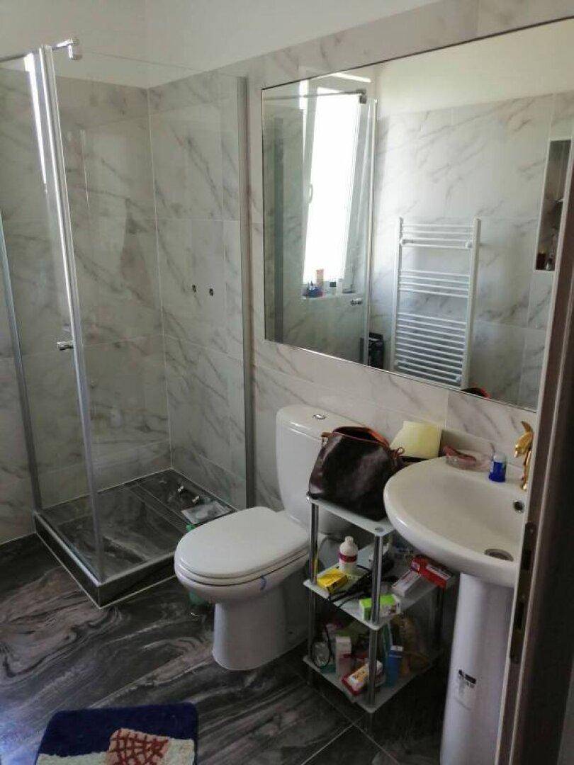 Modernes Badezimmer mit Marmoroptik-Fliesen, Duschkabine und großem Spiegel.