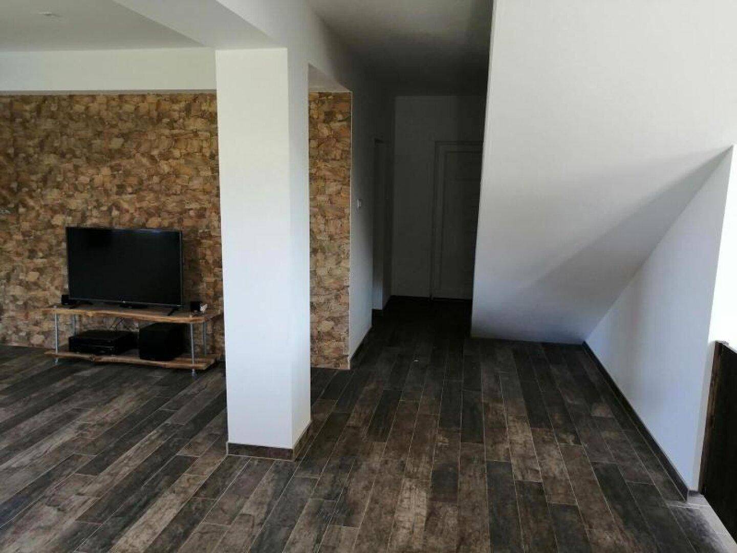 Flur mit Holzoptik-Fliesen und Steinwand, der zum hinteren Bereich des Hauses führt.